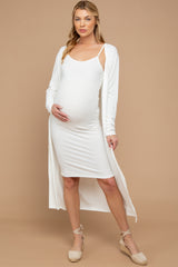 woman wearing a white ribbed maternity dress and a long white cardigan, holding her baby bump
