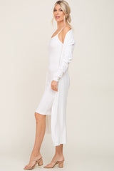woman wearing a white ribbed midi dress with spaghetti straps and a long sleeve cover-up, styled with beige block heel sandals