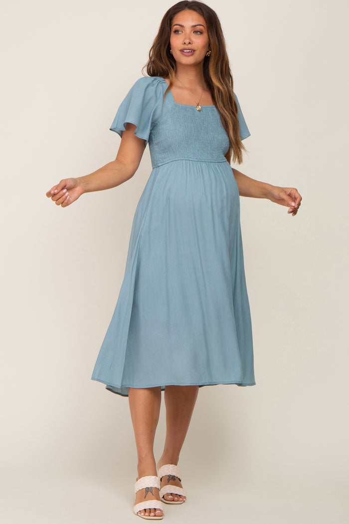 woman wearing a light blue maternity dress with short flutter sleeves and a square neckline, showcasing her baby bump