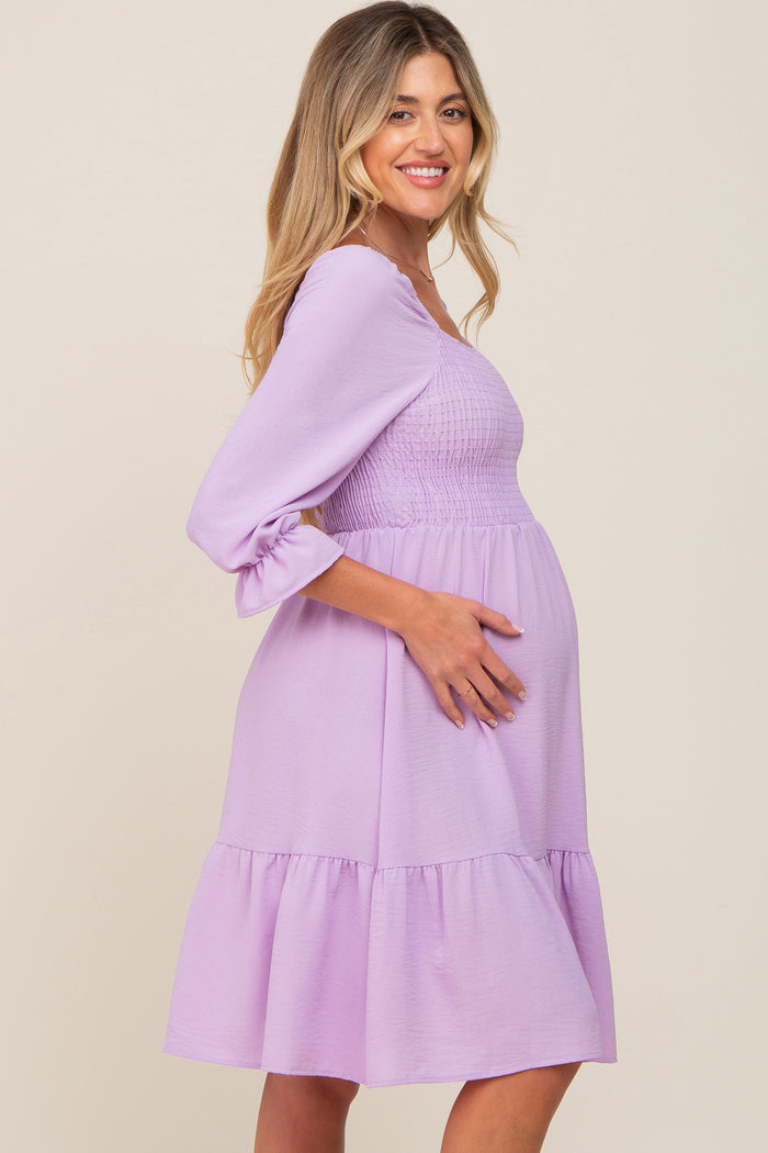 woman wearing a lavender maternity dress with a smocked bodice and ruffled hem, showing her baby bump