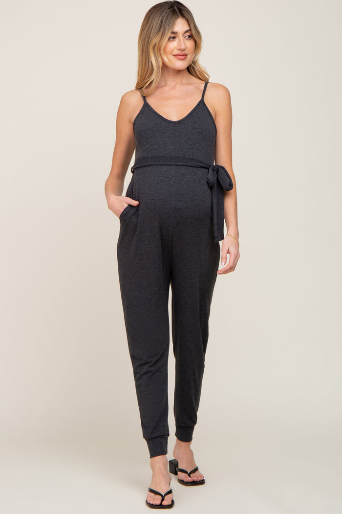 woman wearing a black maternity jumpsuit with adjustable straps and a tie at the waist, showing her baby bump