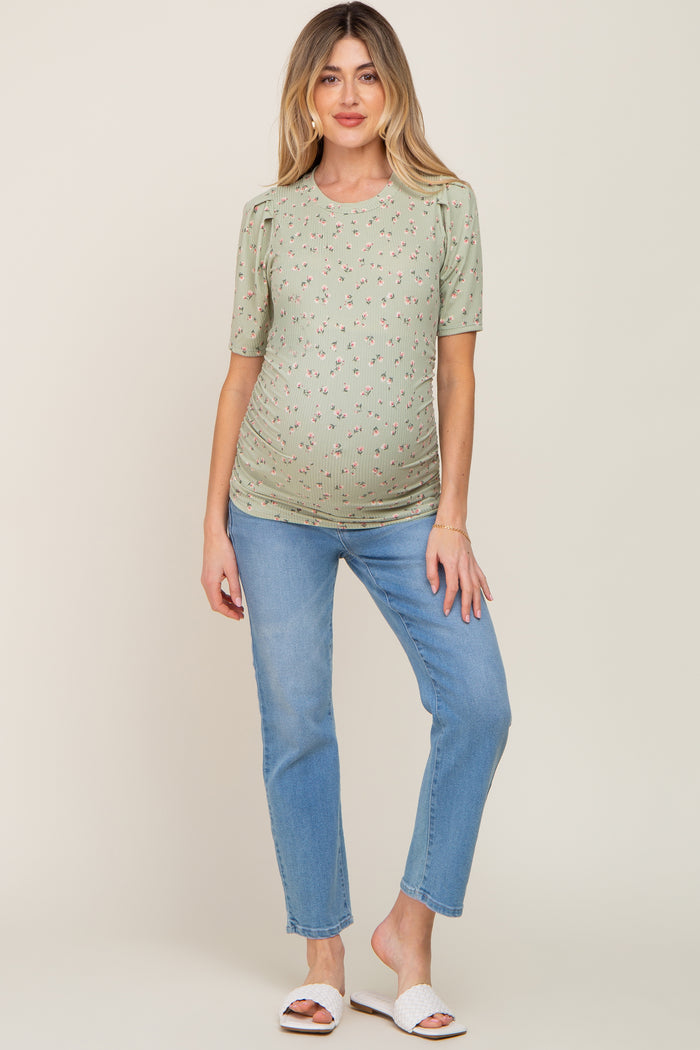 woman wearing a green short sleeve maternity top with floral print and paired with light blue jeans, showing her baby bump