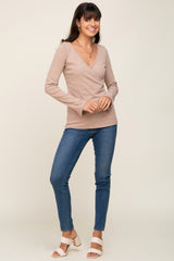 woman wearing a beige long sleeve wrap top paired with blue skinny jeans and white heeled sandals