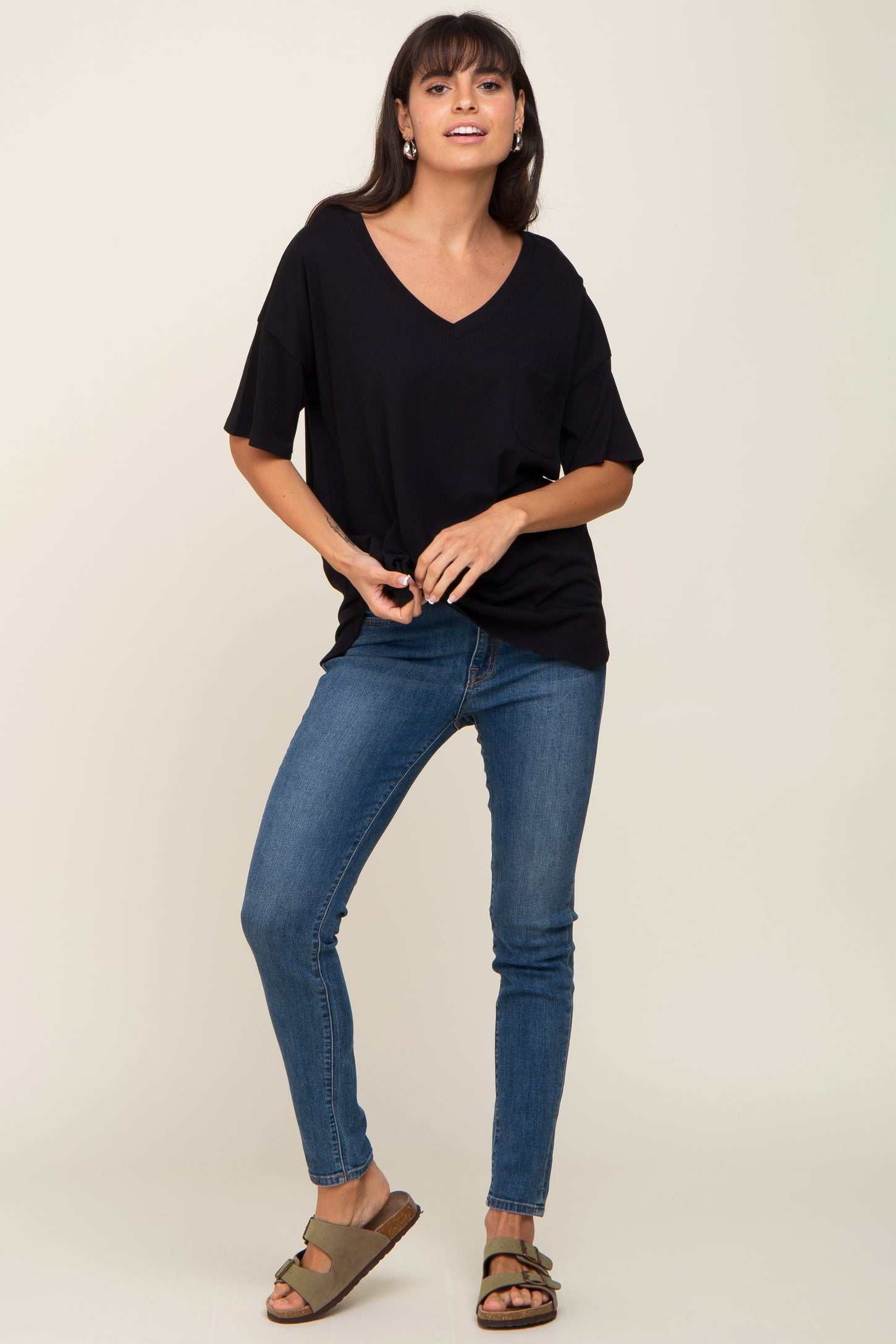 woman wearing a black v-neck loose fit top paired with blue skinny jeans and brown sandals