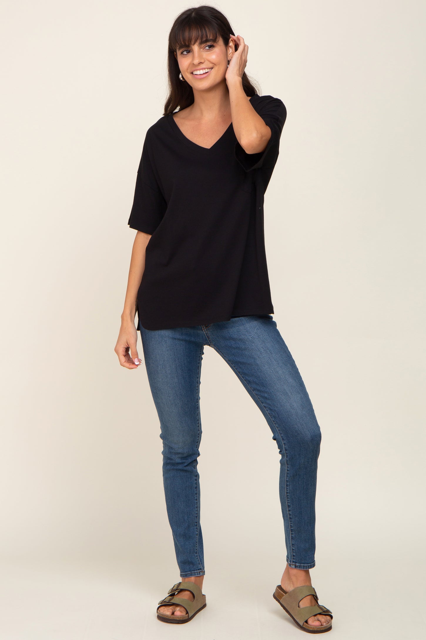 woman wearing a black v-neck oversized t-shirt and blue skinny jeans, smiling and posing with one hand in her hair