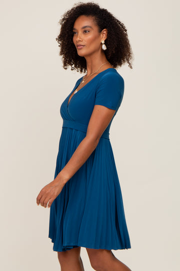 woman wearing a teal short sleeve dress with a fitted bodice and flared skirt, styled with curly hair and earrings