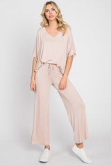 woman wearing a loose-fitting light pink jumpsuit with a v-neck and wide-leg pants, paired with white sneakers