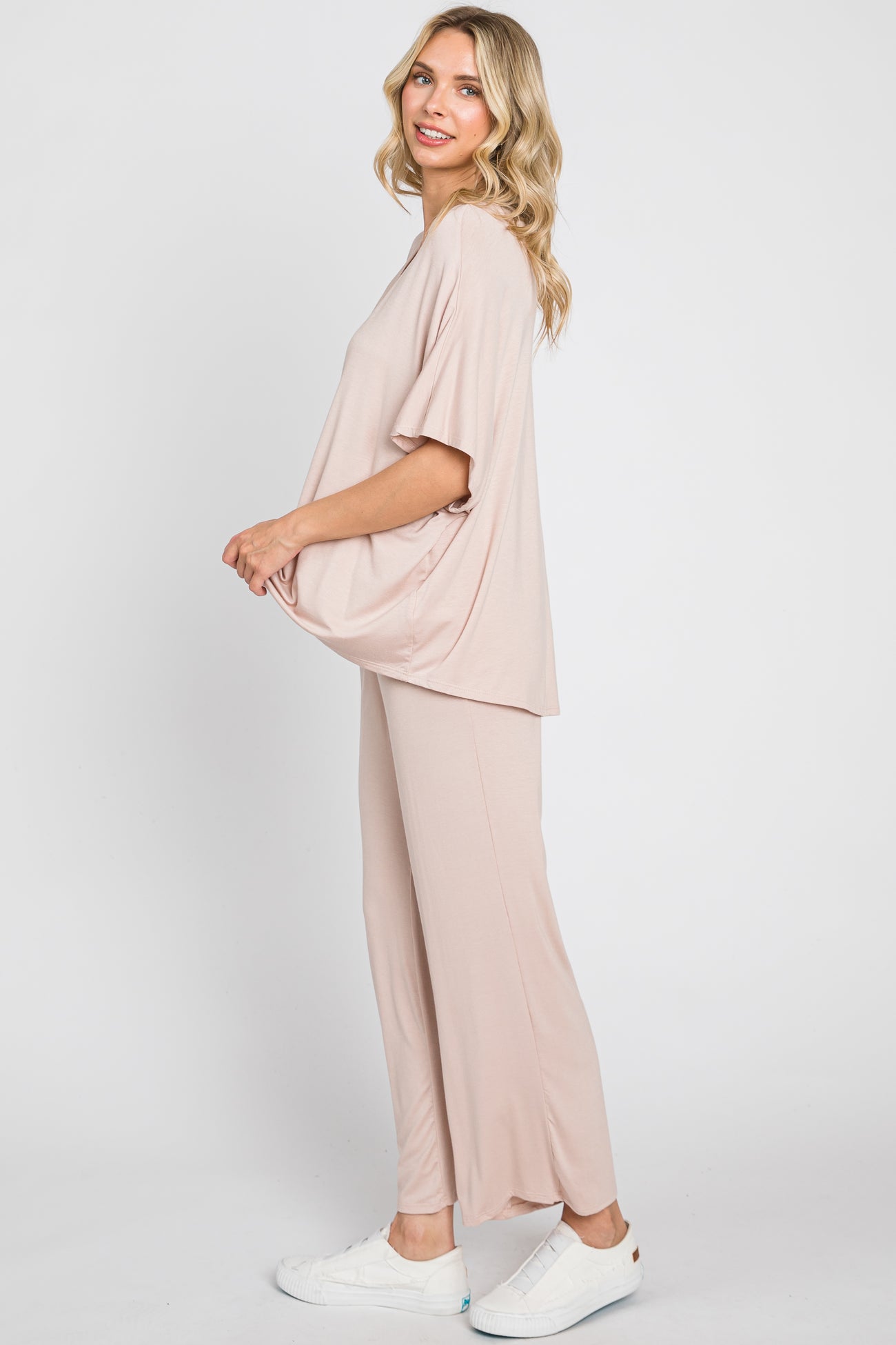 woman wearing a light pink oversized top and matching flowy pants with white sneakers