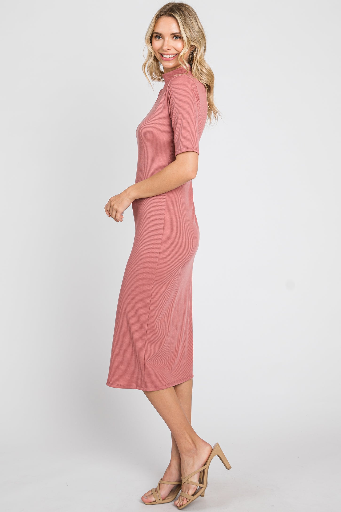 woman wearing a dusty rose ribbed midi dress with short sleeves and a high neckline, standing sideways in sandals