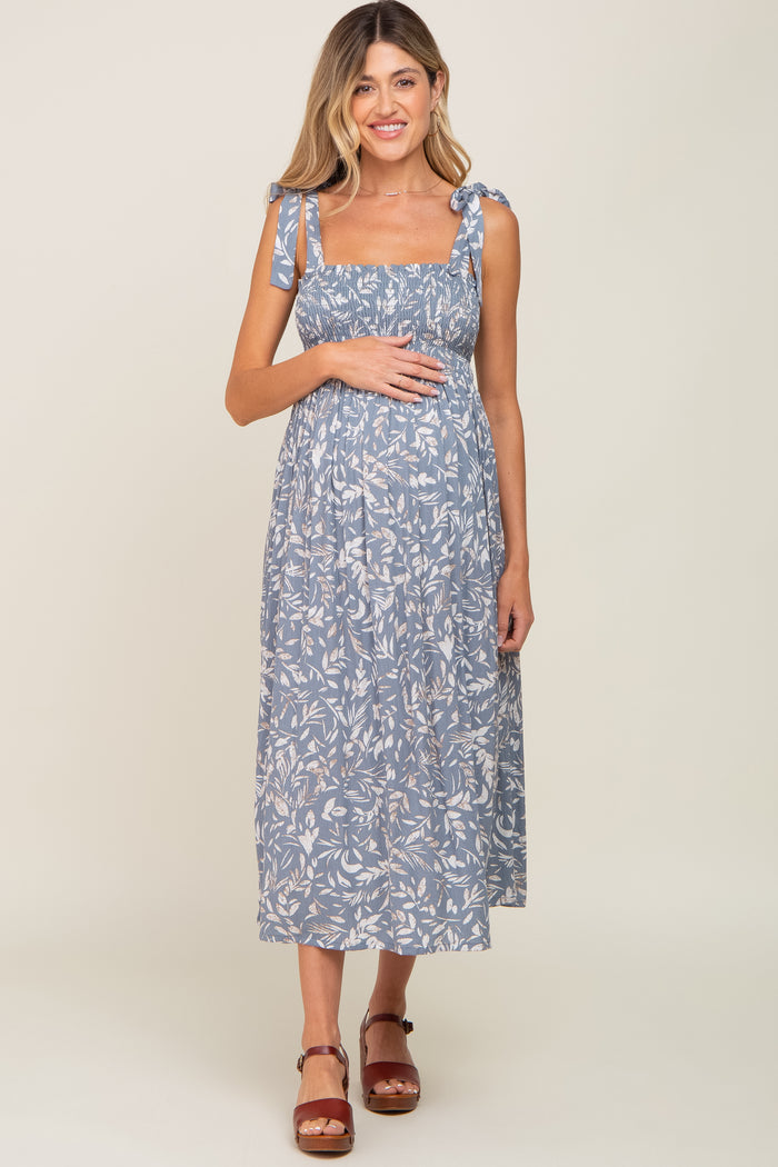 woman wearing a blue floral maternity dress with tie shoulder straps and holding her baby bump