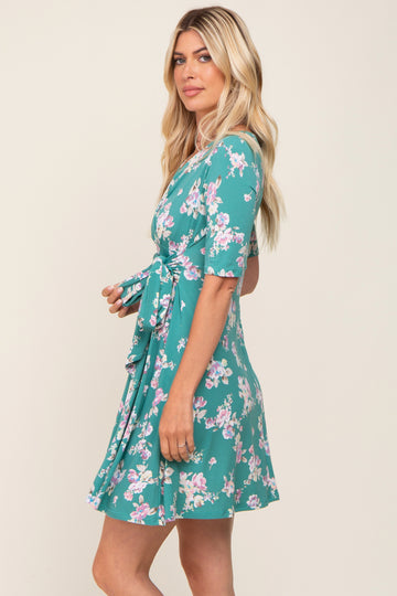 Woman wearing a teal floral print short sleeve wrap dress with a waist tie