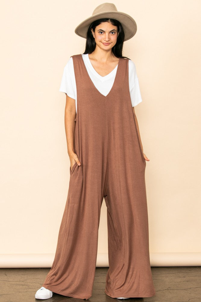 woman wearing a brown wide leg jumpsuit over a white t-shirt and a tan wide brim hat