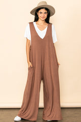 woman wearing a brown wide leg jumpsuit over a white t-shirt and a tan wide brim hat