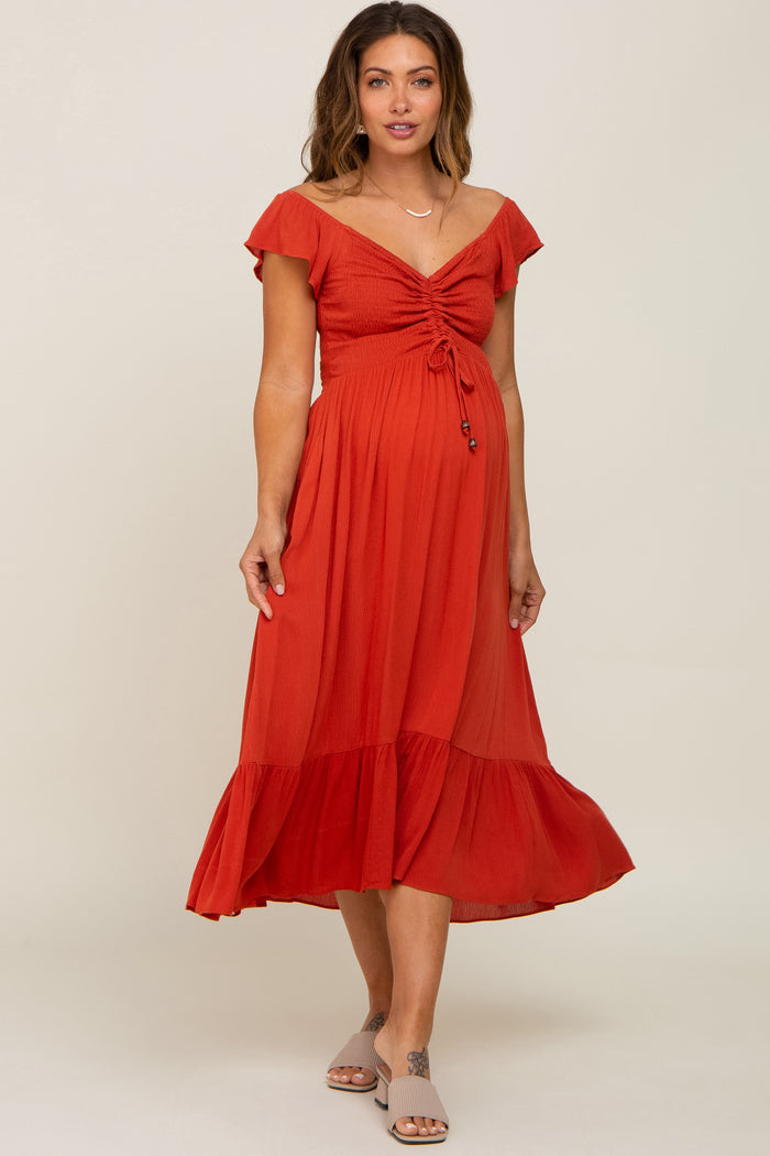 woman wearing a rust red maternity dress with a tie front and flutter sleeves, showcasing her baby bump