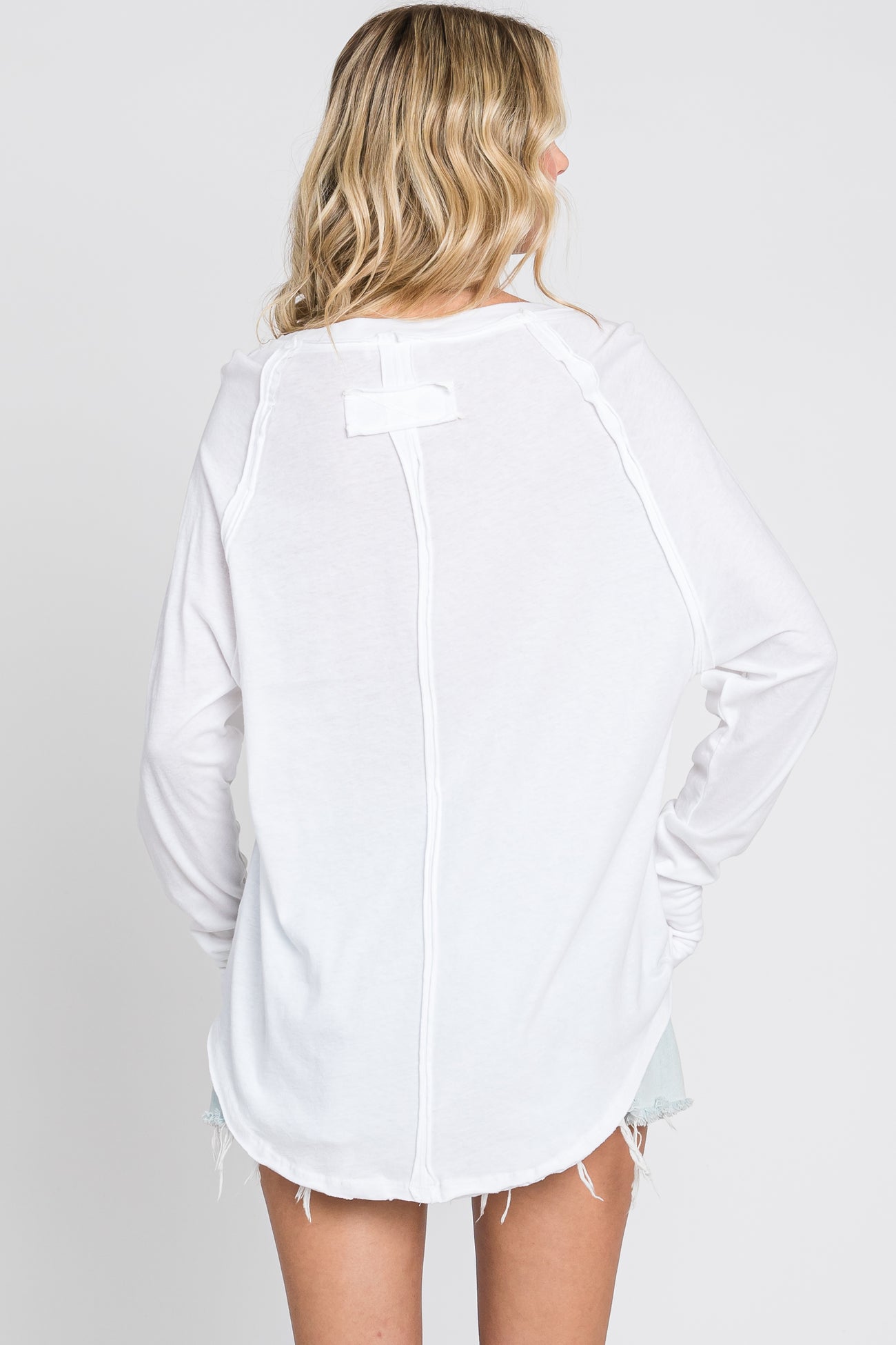 woman wearing a white long sleeve top with a scoop back and raw hem detail, shown from the back