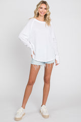 woman wearing a white long sleeve oversized top with distressed hem and casual denim shorts, styled with platform sneakers