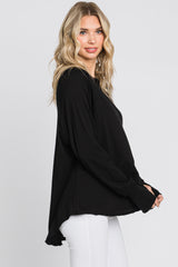 woman wearing a black long sleeve oversized top with a relaxed fit and side slit, paired with white pants