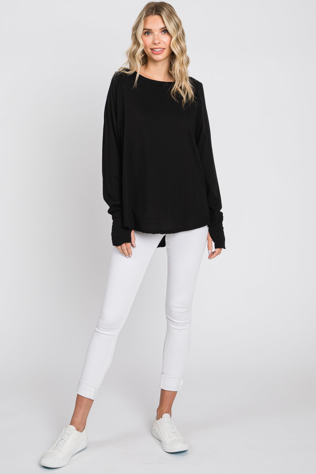 woman wearing a black long sleeve top with relaxed fit and white skinny jeans, paired with white sneakers