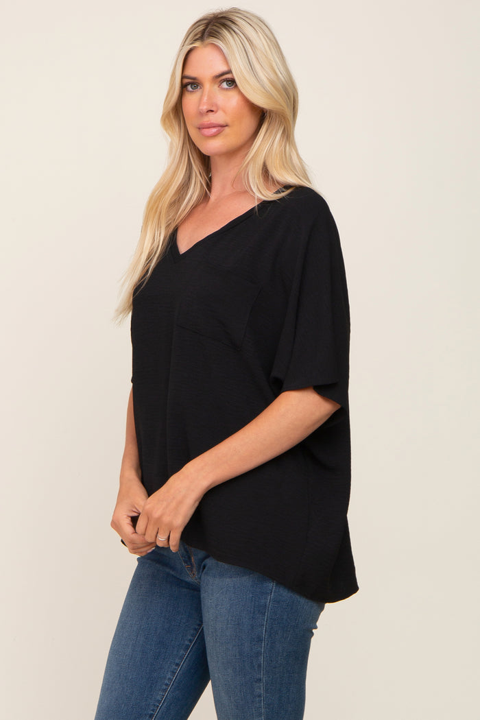 woman wearing a black v-neck oversized top with a front pocket and relaxed fit, paired with blue jeans
