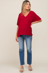 woman wearing a red v-neck maternity top and distressed blue jeans with a visible baby bump