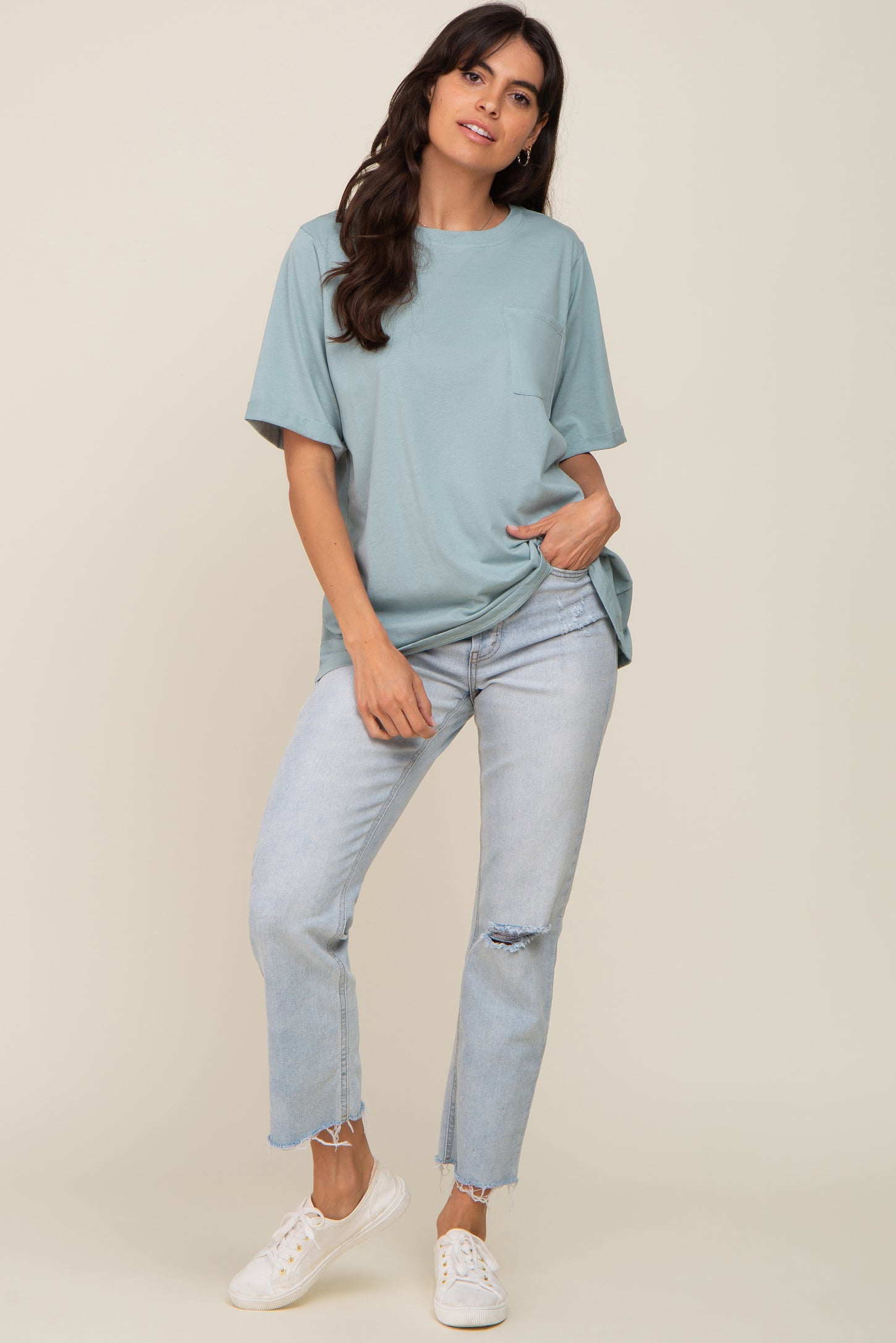 woman wearing a teal oversized t-shirt with a pocket and light wash ripped jeans, standing in casual pose