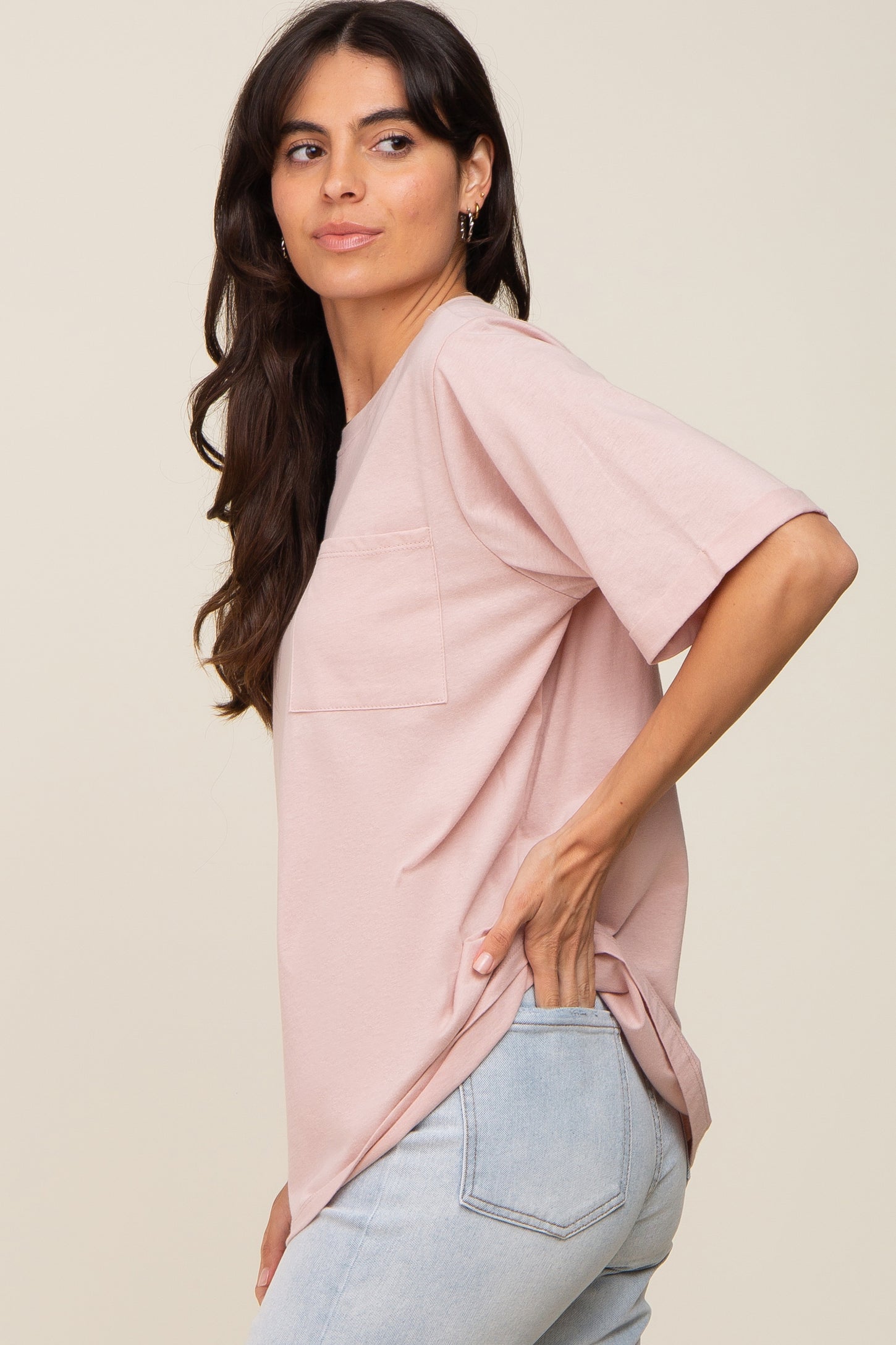 woman wearing a light pink oversized short sleeve t-shirt with a pocket and styled with high-waisted jeans