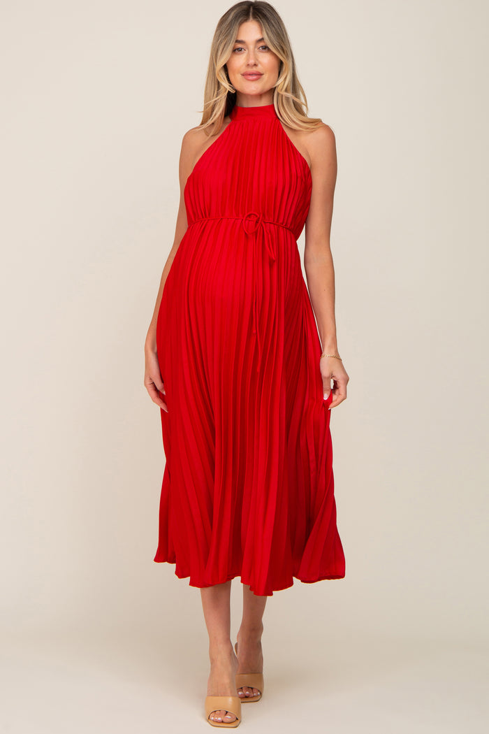 woman wearing a red pleated maternity dress with a halter neck and tied waist, showcasing her baby bump