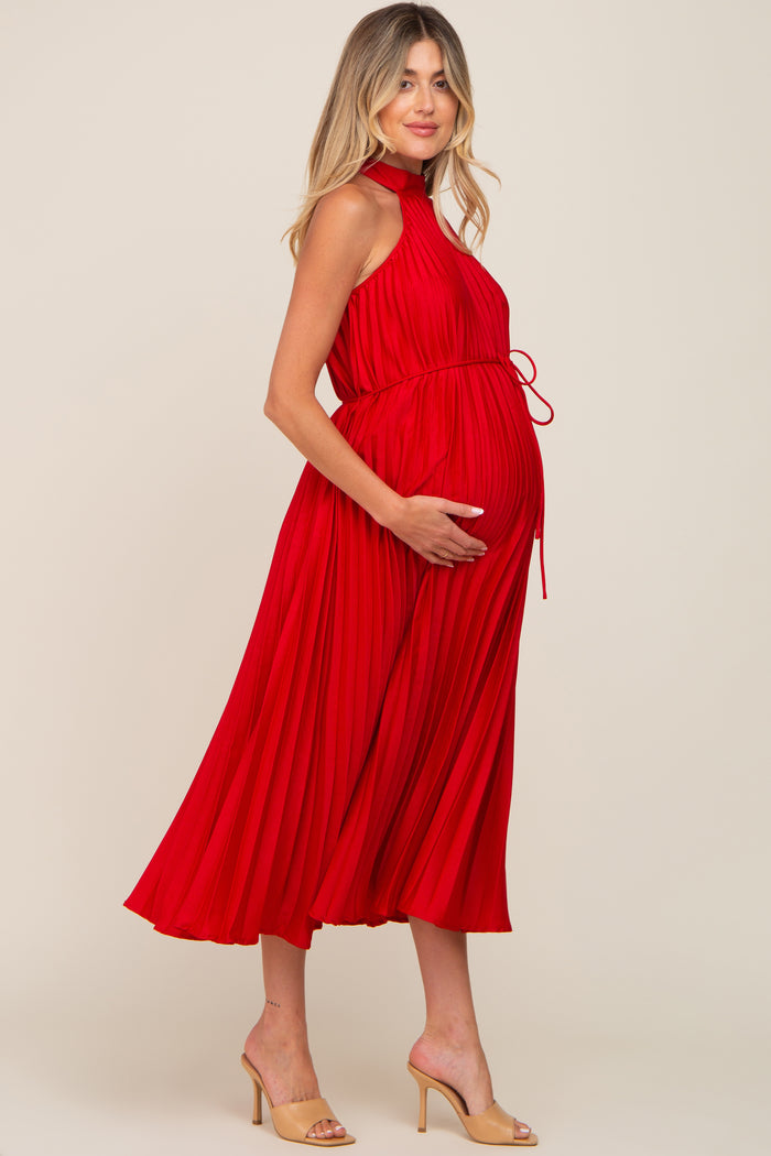 woman wearing a red pleated maternity dress with a tie waist, showcasing her baby bump