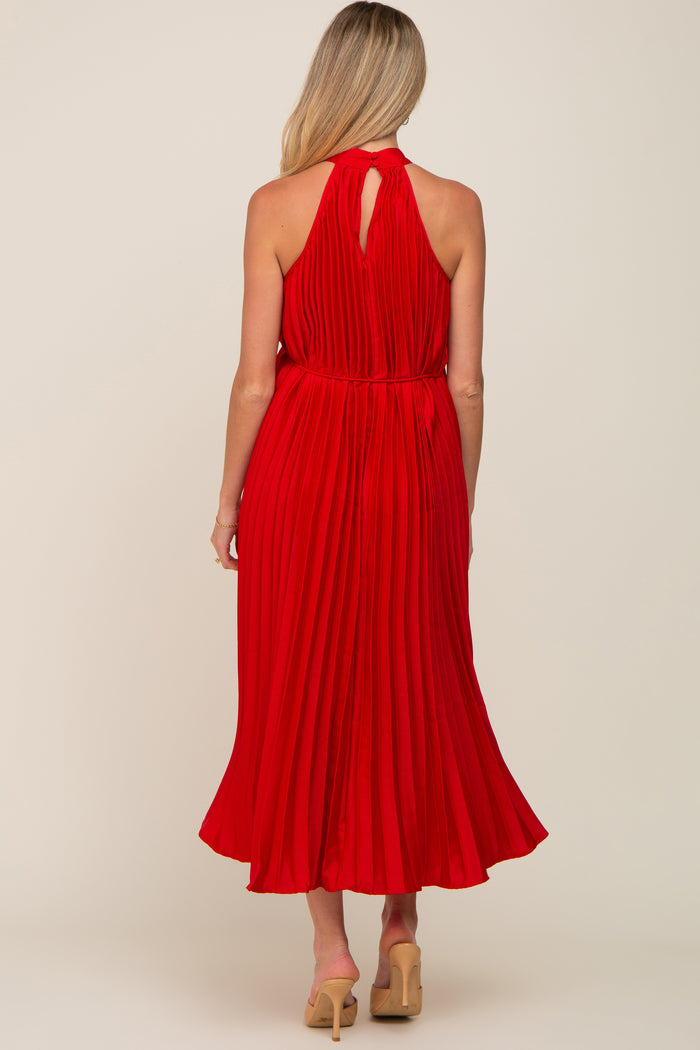 woman wearing a red pleated maternity dress with a halter neck and flowing skirt from the back