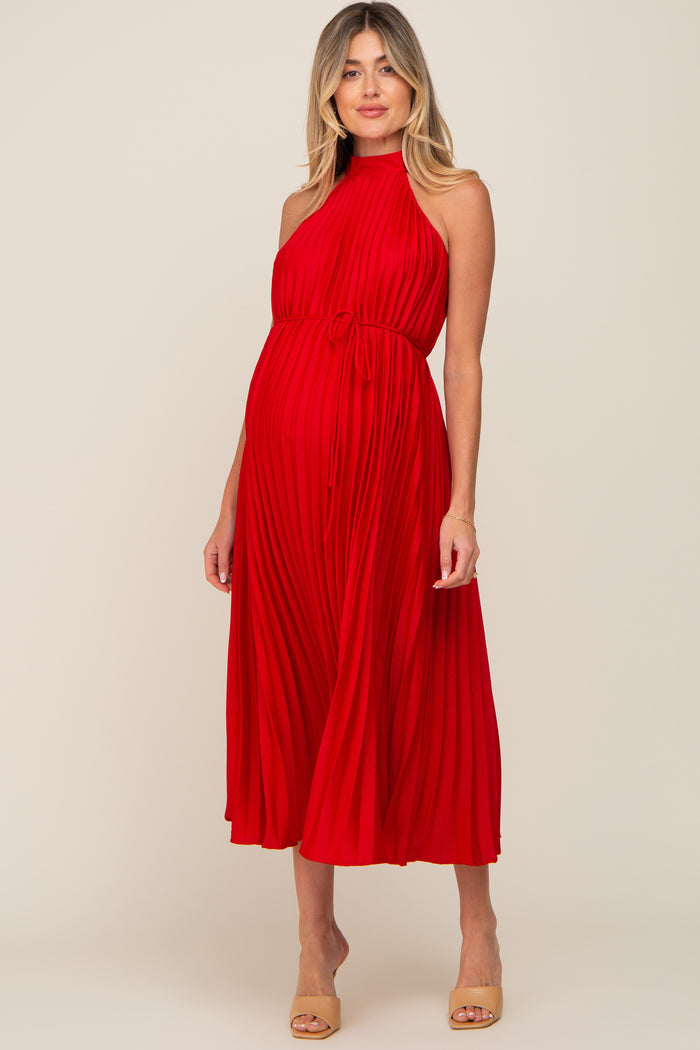 woman wearing a red pleated maternity dress with a halter neck and a tie at the waist, showcasing her baby bump