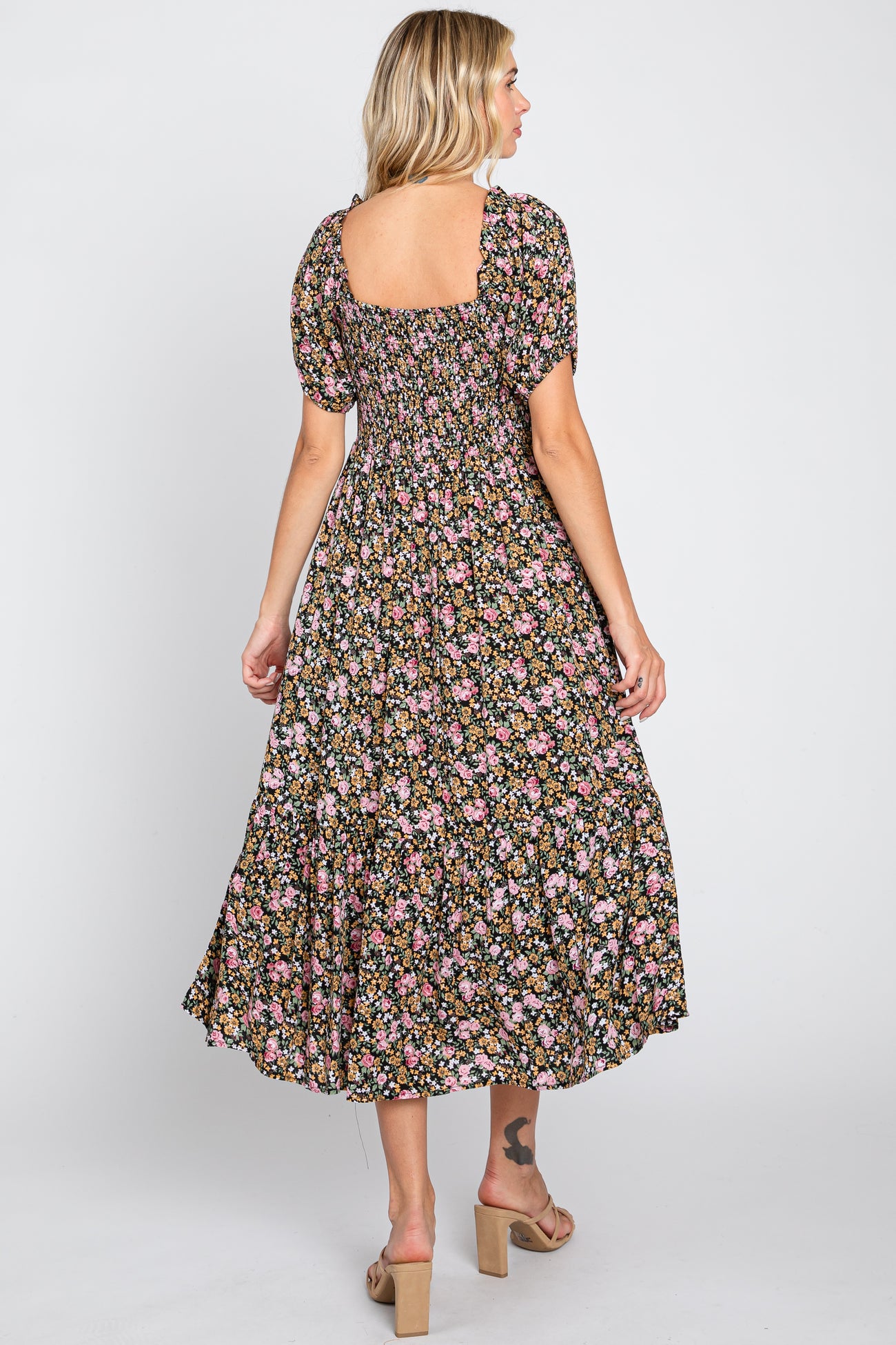 woman wearing a black floral midi dress with short puff sleeves and a square neckline, standing with her back to the camera