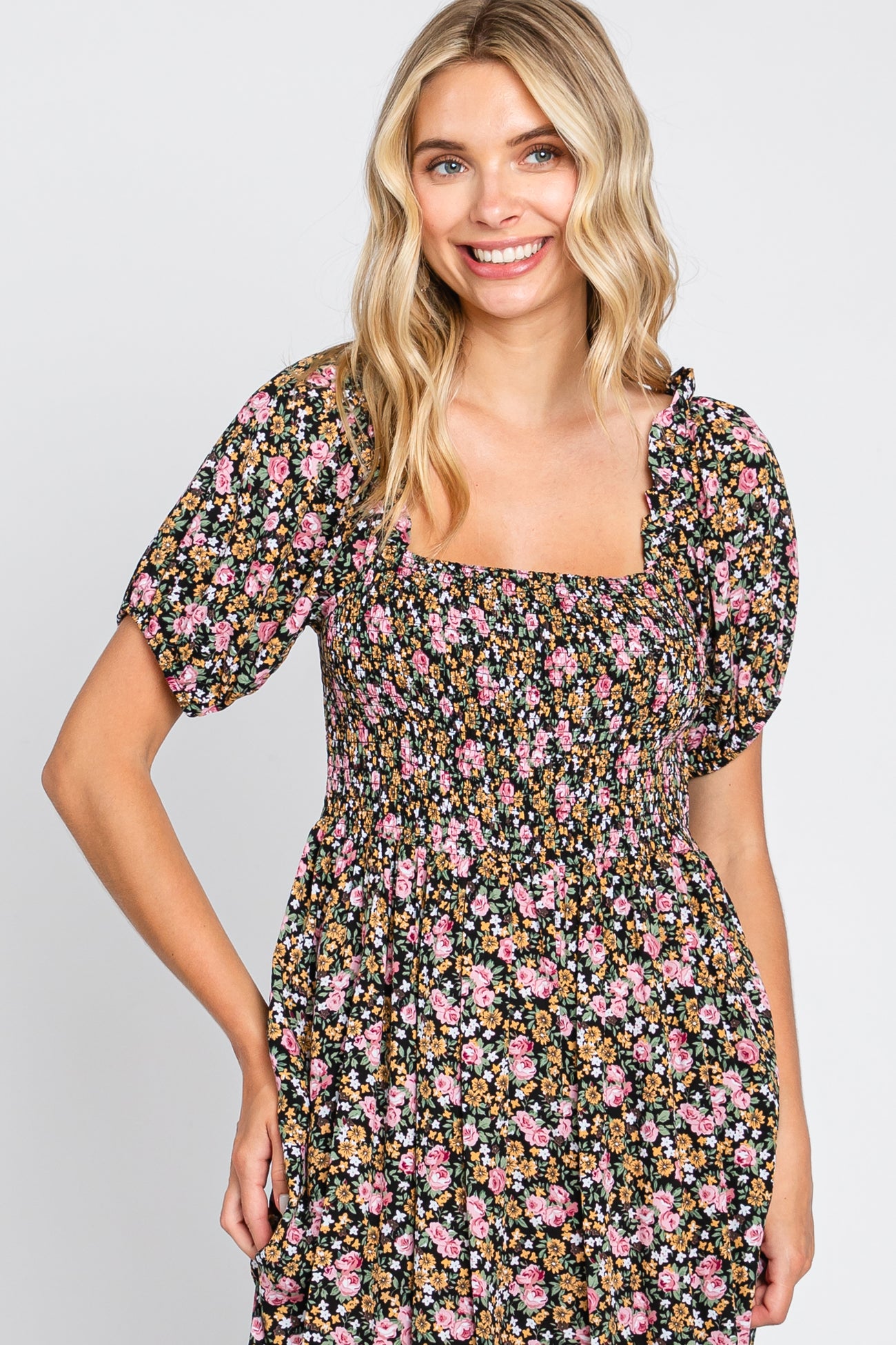 woman wearing a black floral square neck dress with puff sleeves and smocked bodice, smiling at the camera