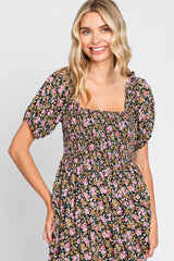 woman wearing a black floral square neck dress with puff sleeves and smocked bodice, smiling at the camera