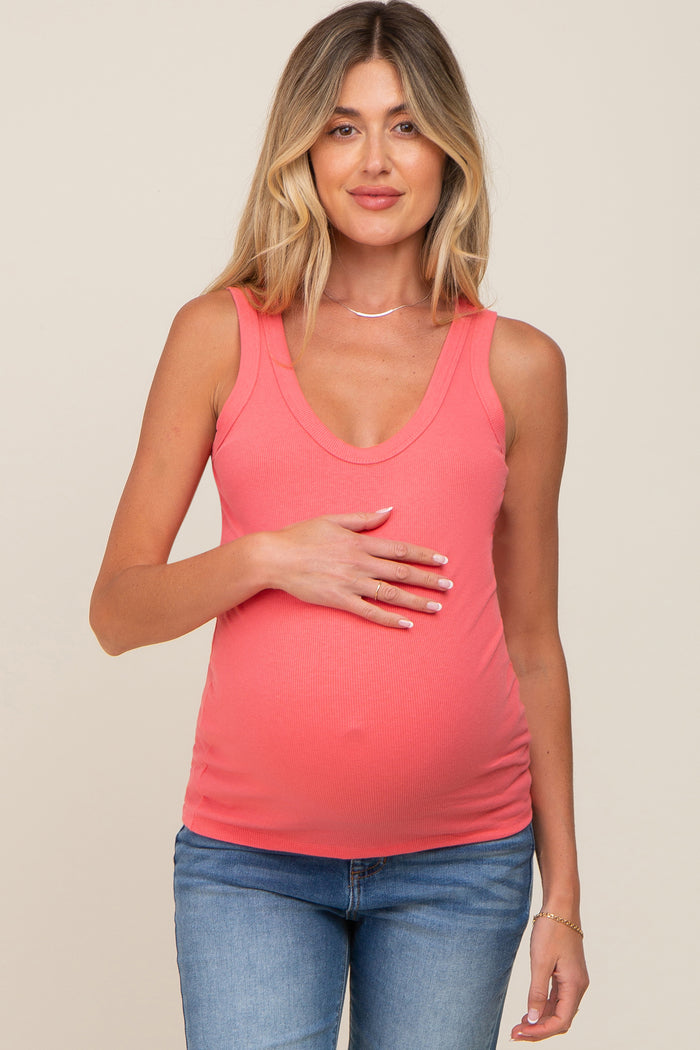 pregnant woman wearing a coral ribbed maternity tank top and blue jeans holding her baby bump