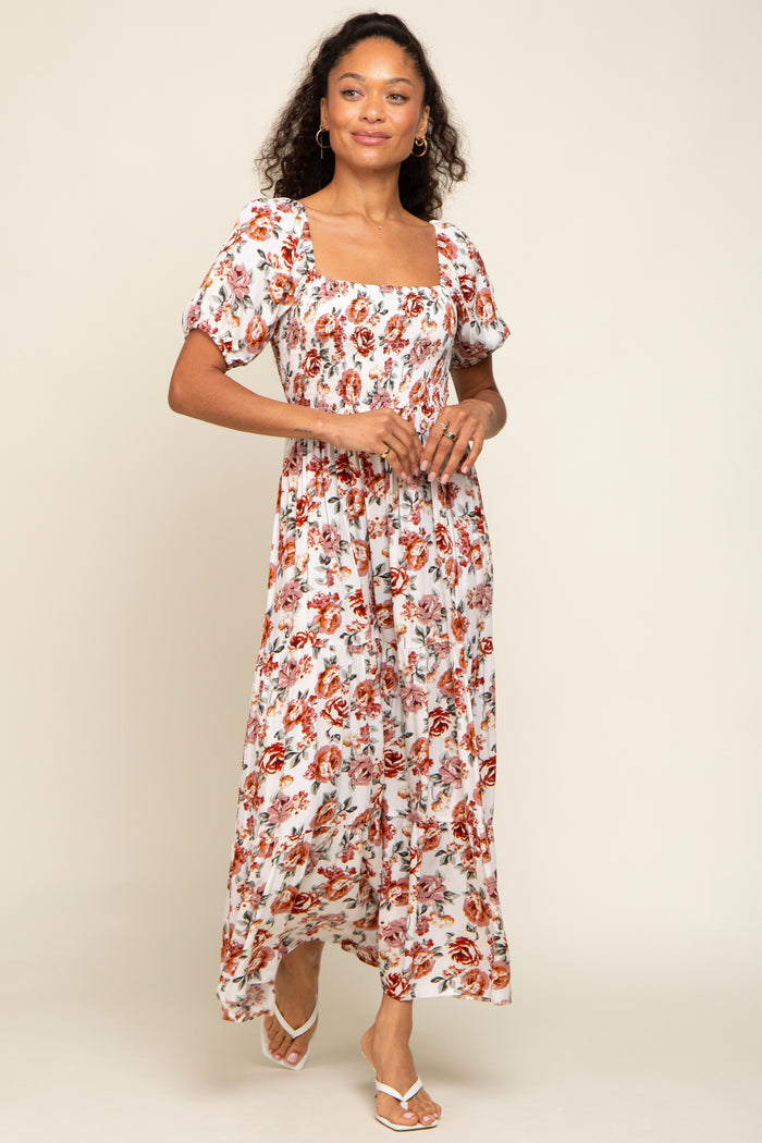 woman wearing a white floral maxi dress with short puff sleeves and a square neckline, smiling against a neutral background