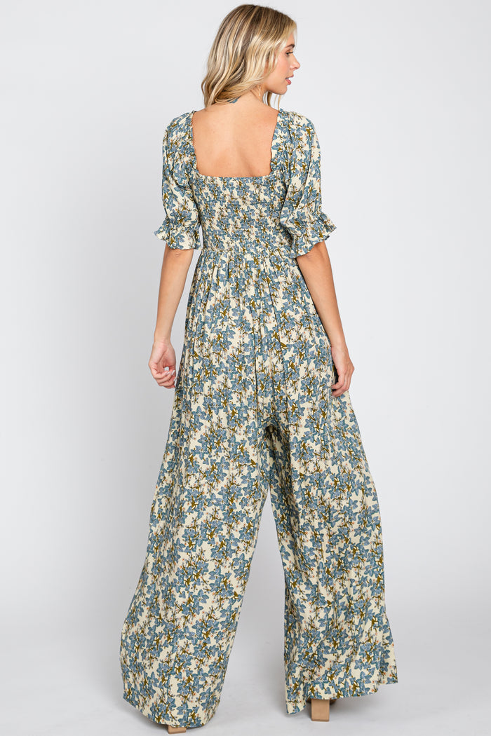 Back view of a woman wearing a blue floral print wide leg jumpsuit with smocked bodice and ruffled sleeves