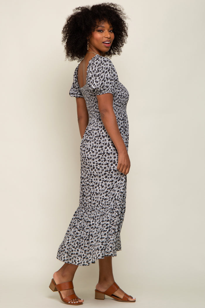 woman wearing a black and white floral midi dress with short puff sleeves and a ruffled hem, standing sideways