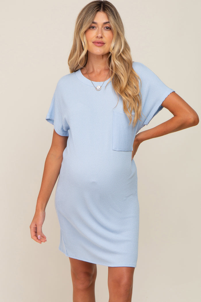 woman wearing a light blue maternity dress with short sleeves and a chest pocket, showing her baby bump