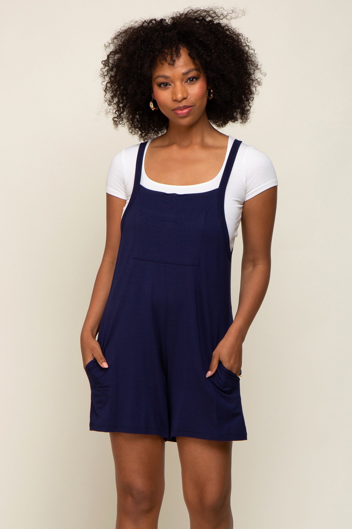 woman wearing a navy blue romper with pockets over a white fitted t-shirt and styled with curly hair