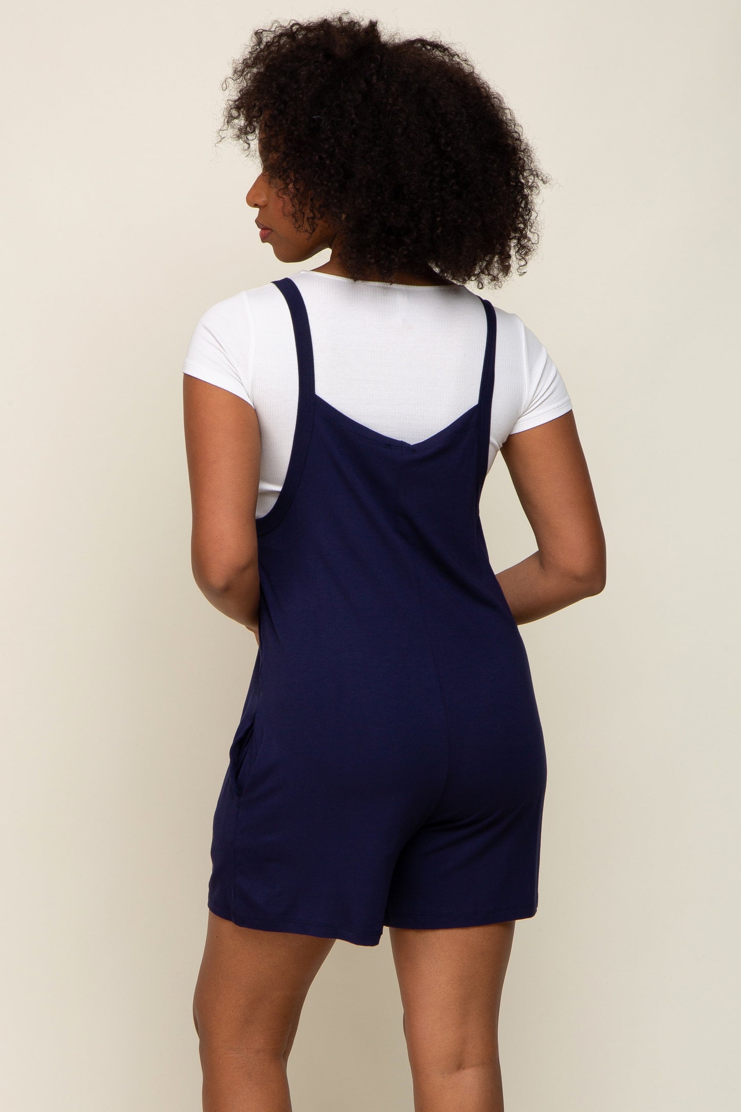 woman wearing a navy blue romper with adjustable straps and pockets, shown from the back