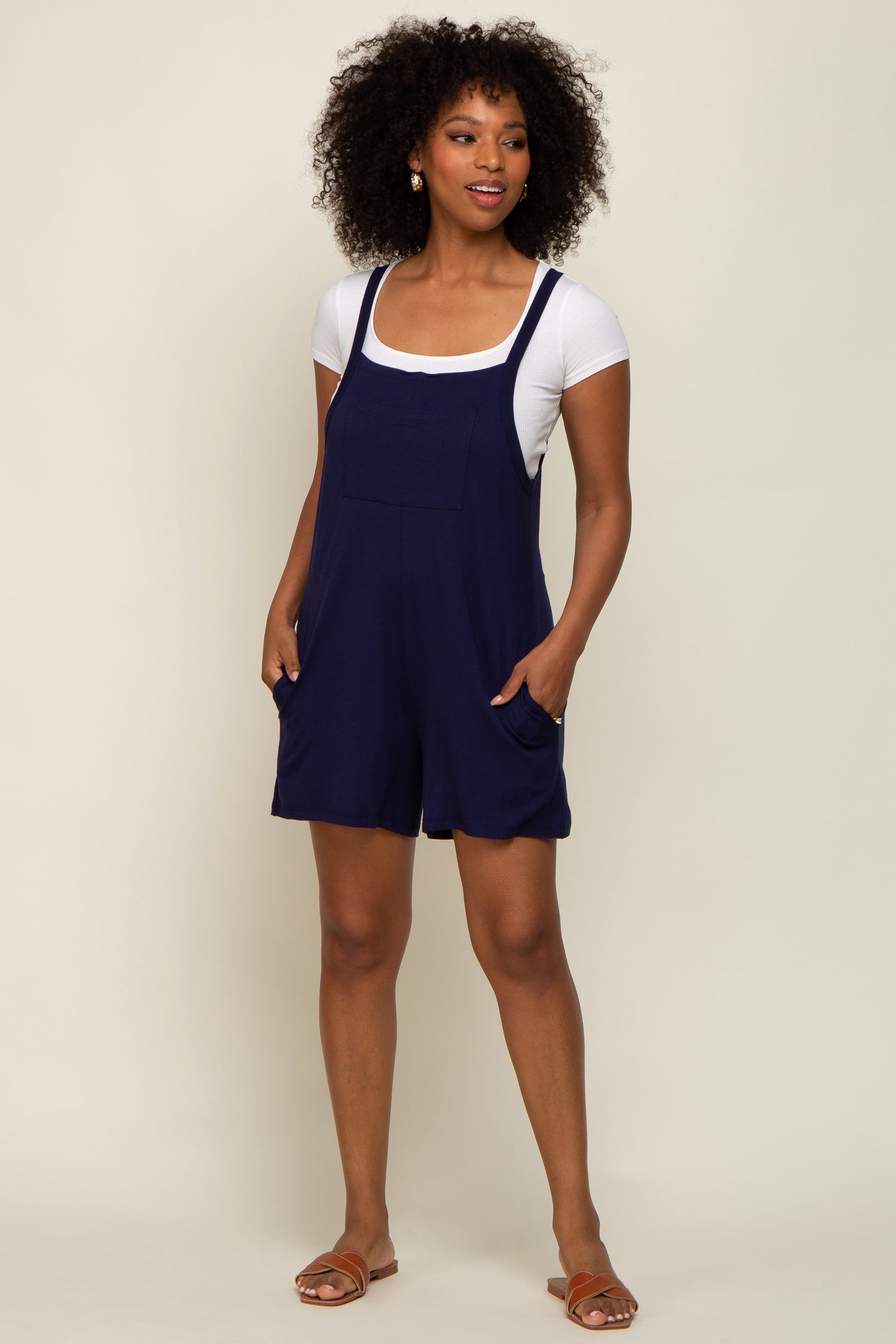 woman wearing a navy blue sleeveless romper with pockets and a white t-shirt underneath