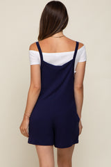 woman wearing a navy blue maternity romper with straps over a white top, showing the back view