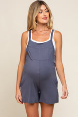 pregnant woman wearing blue maternity overalls over a white tank top