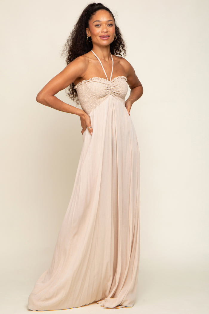 woman wearing a light beige strapless maxi dress with smocked bodice and flowing skirt, posing confidently