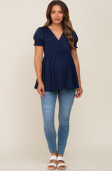 woman wearing a navy blue maternity top with puff sleeves and a fitted empire waist, paired with light blue skinny jeans