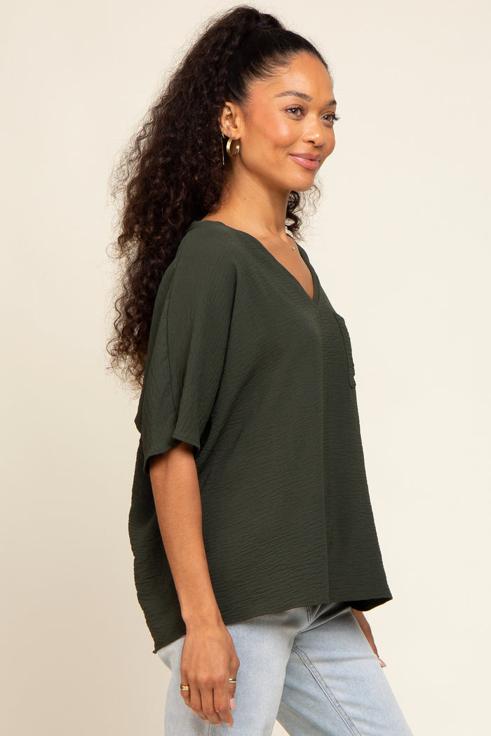 woman wearing a dark green v-neck short sleeve textured blouse and light wash jeans