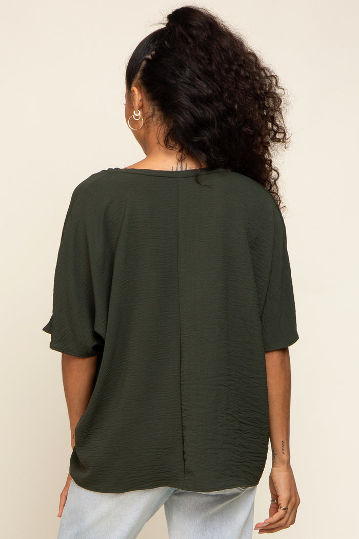 Back view of a woman wearing a dark olive green short sleeve textured blouse and light wash jeans