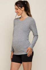 woman wearing a gray long sleeve maternity top and black shorts, showing her baby bump