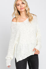 woman wearing an off-white oversized knit sweater with a scooped neckline and side slits, paired with black jeans