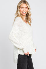 woman wearing a light cream oversized knit sweater paired with dark jeans, smiling and facing slightly to the side